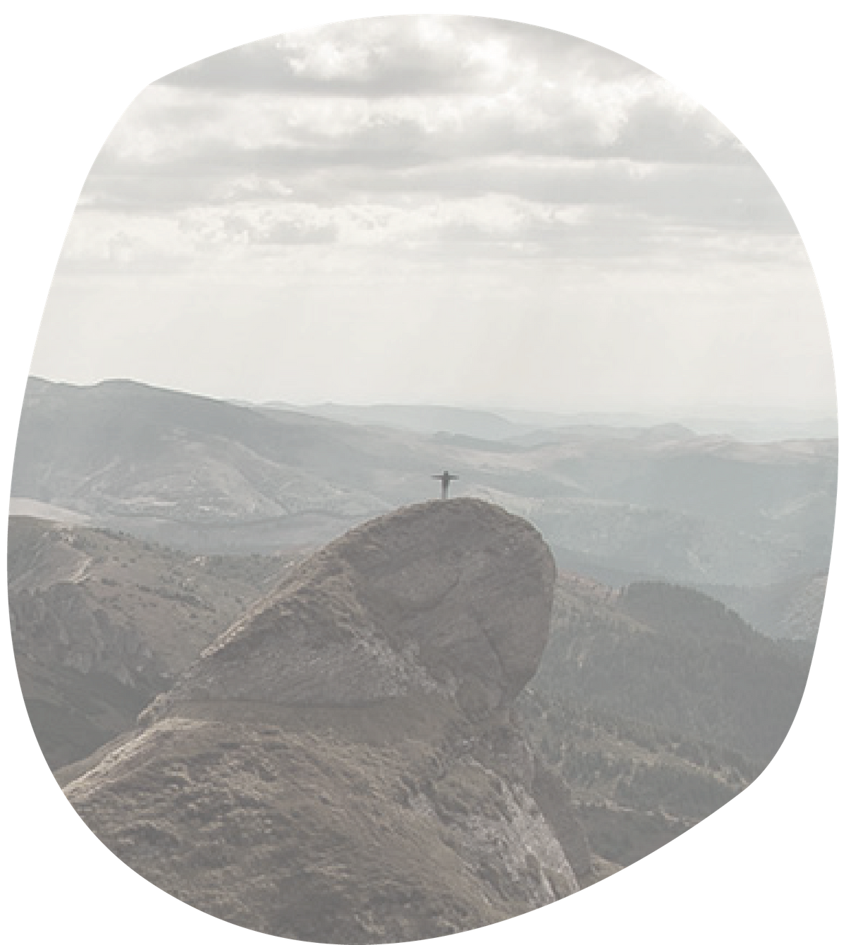 Ein Mensch steht auf einem Gipfel vor einem Bergpanorama und breitet die Arme aus