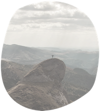 Ein Mensch steht auf einem Gipfel vor einem Bergpanorama und breitet die Arme aus